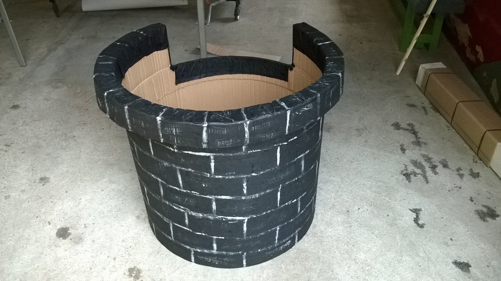 Ein schwarzer Blumentopf aus Ziegeln steht auf einem Betonboden