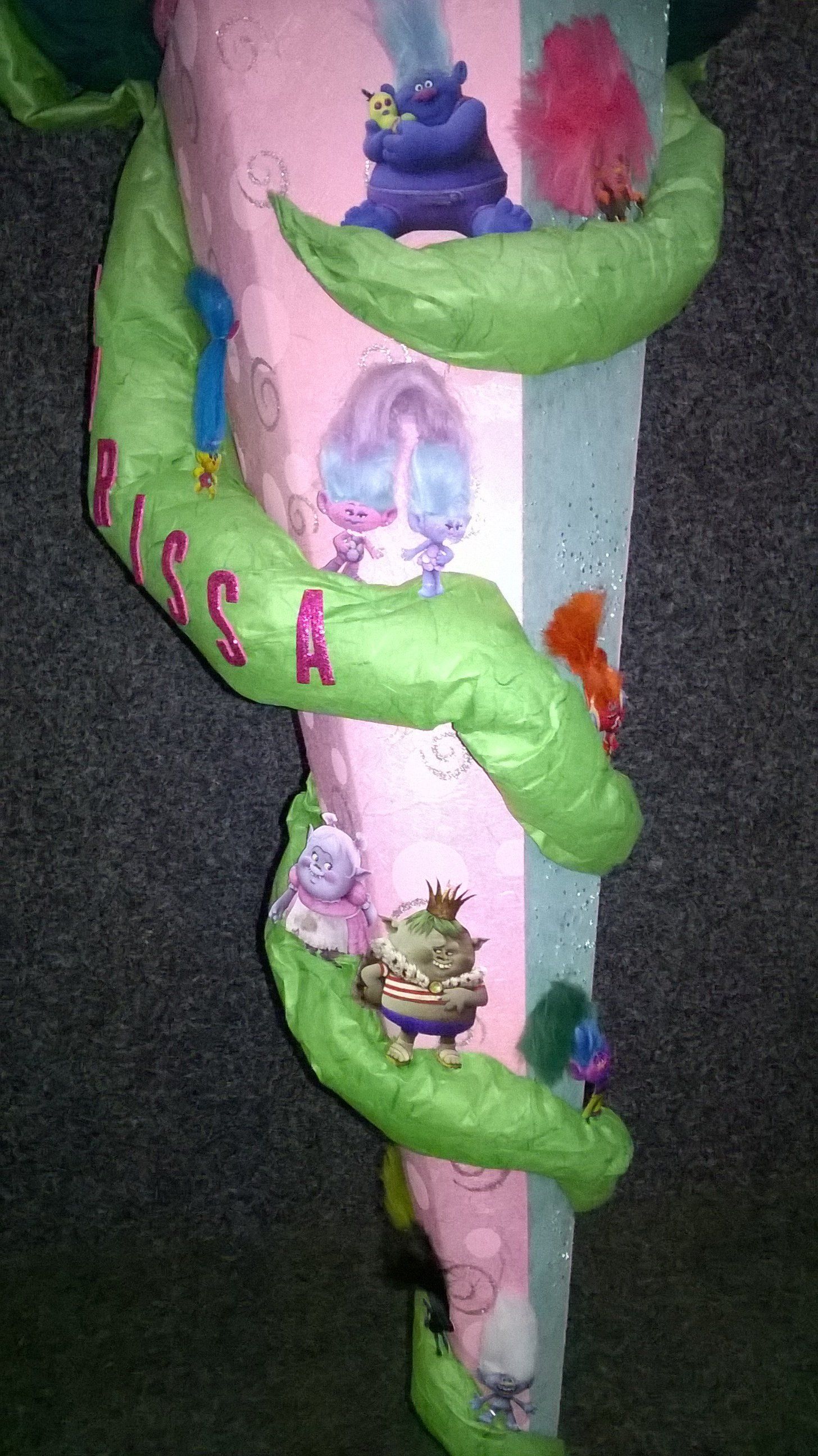 Eine rosa-grüne Skulptur mit Trollen darauf sitzt auf einem Teppich.