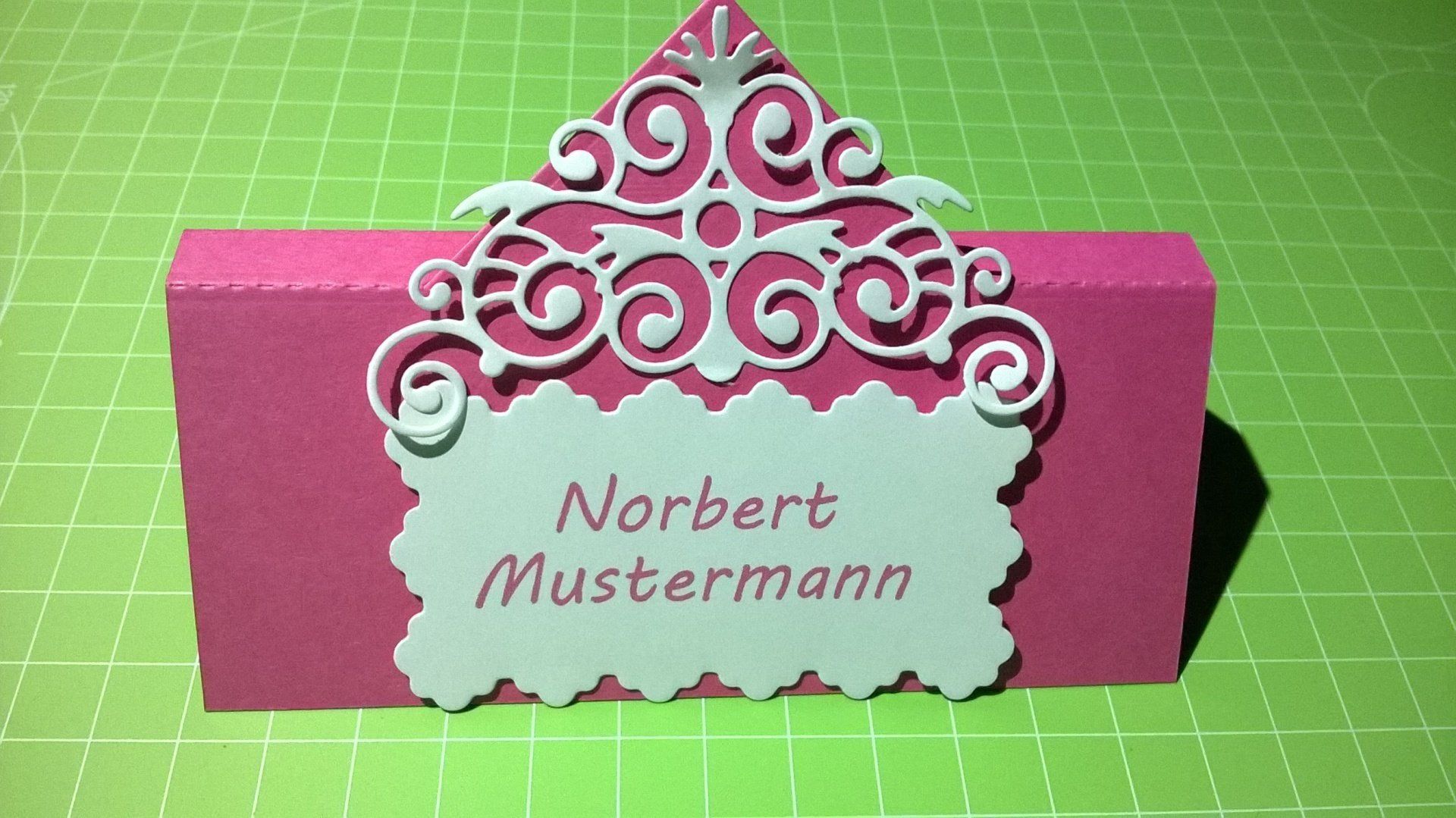 Eine rosa-weiße Tischkarte mit dem Namen Norbert Mustermann darauf