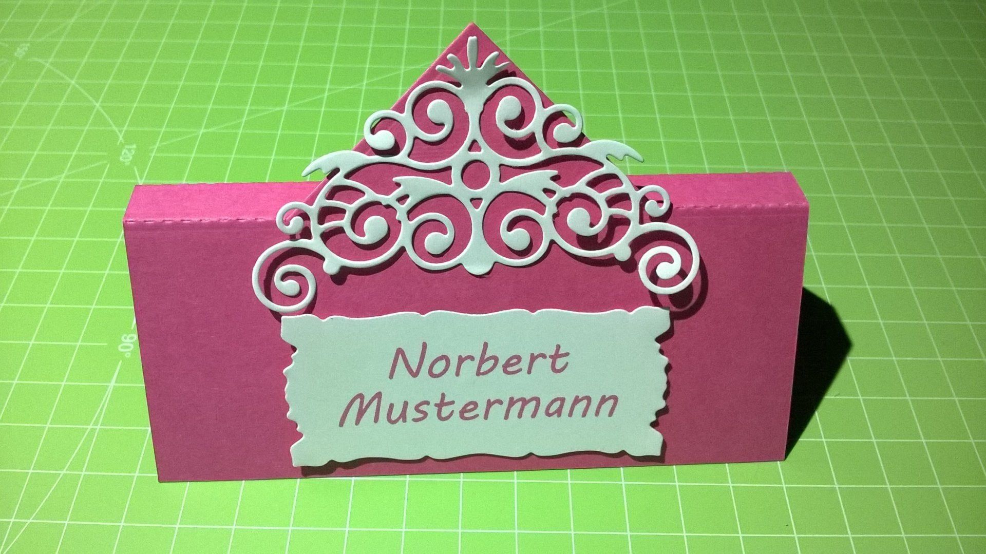Eine rosa-weiße Tischkarte mit dem Namen Norbert Mustermann darauf