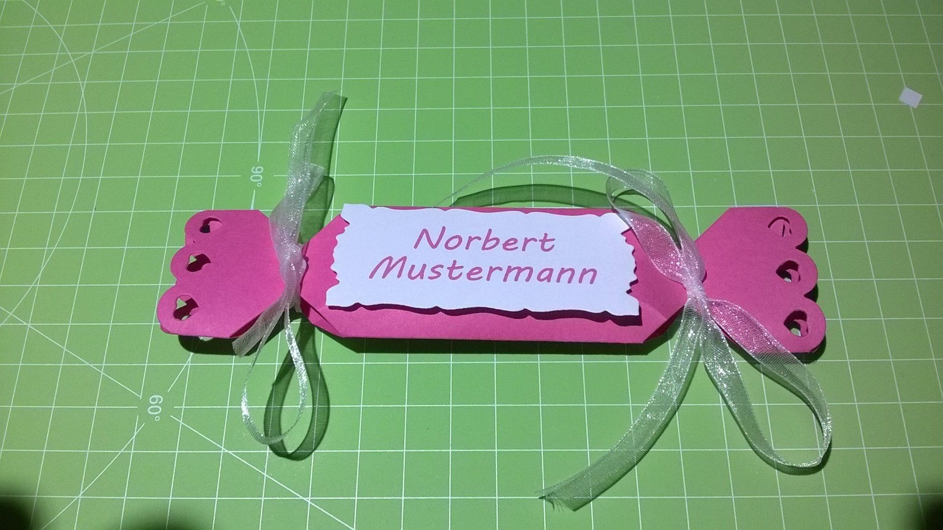 Ein rosa Bonbon mit einem Namensschild liegt auf einem grünen Schneidebrett.