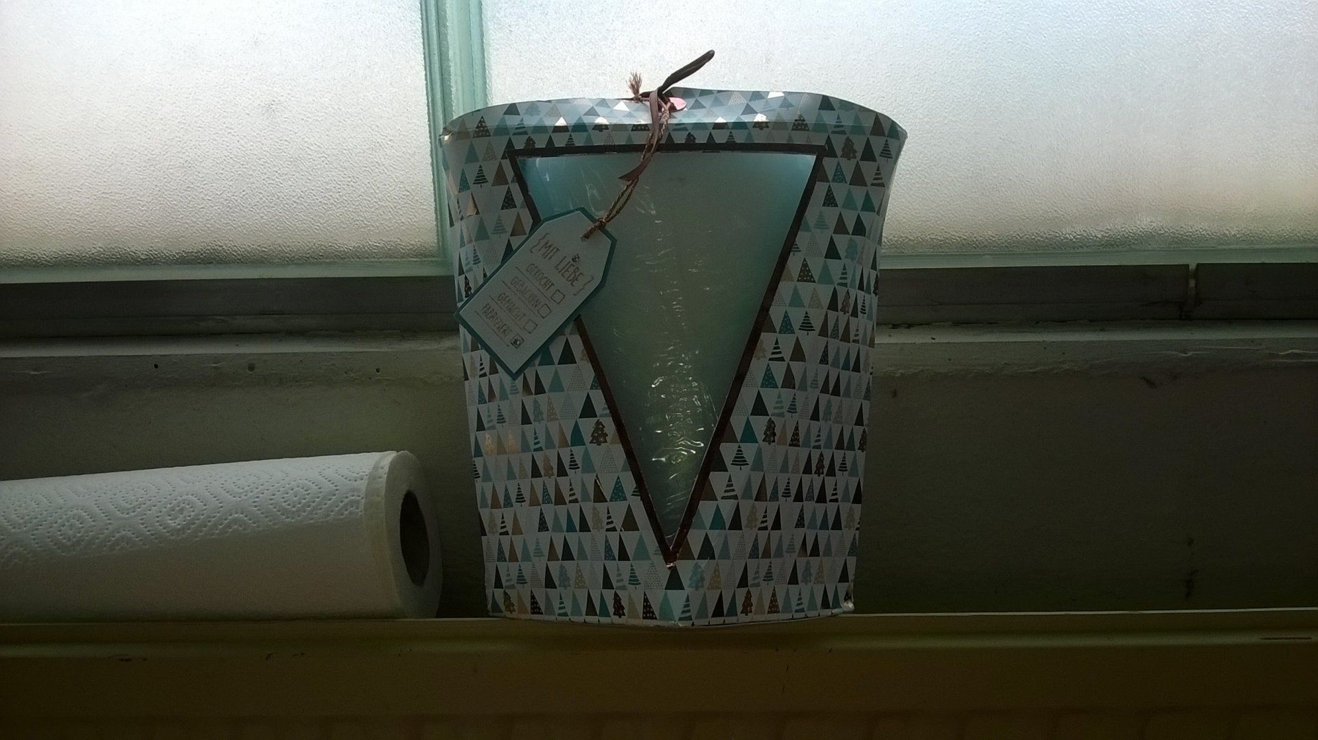 Eine Kerze auf einem Fensterbrett neben einer Rolle Küchenpapier