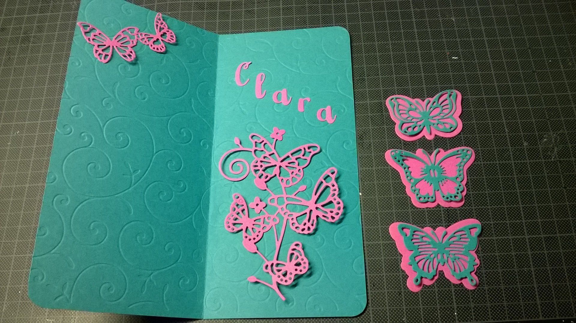Auf einem Tisch liegt eine blaue Karte mit rosa Schmetterlingen darauf.