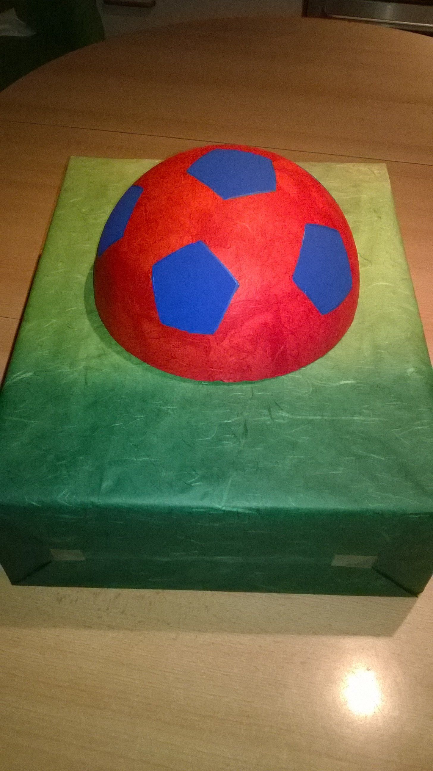 Ein rot-blauer Fußball liegt auf einer grünen Kiste.