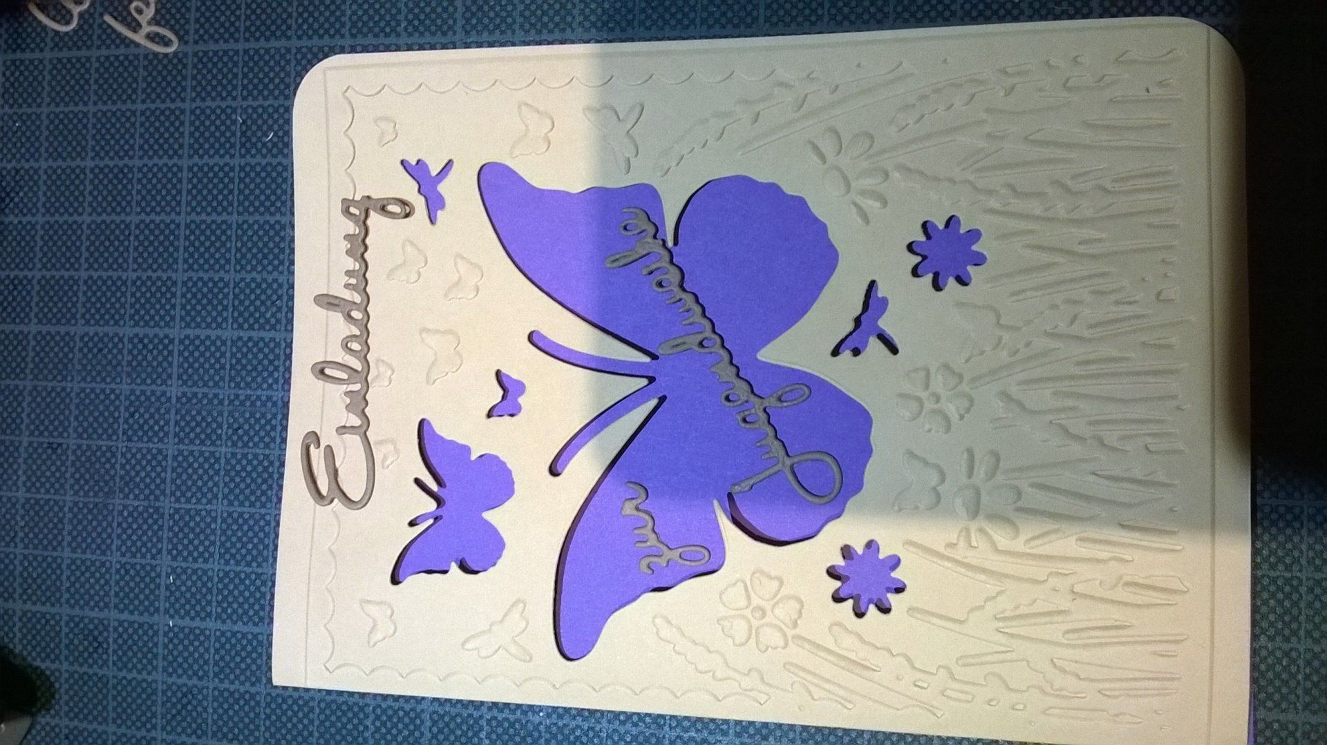 Eine weiße Karte mit einem lila Schmetterling und dem Wort Einladung darauf