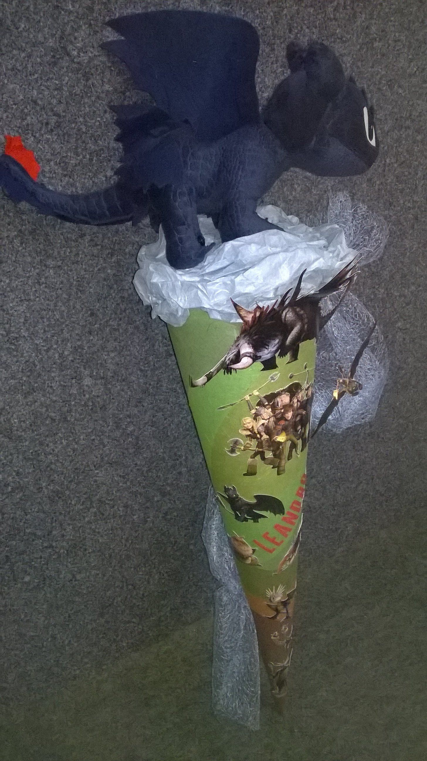 Ein ausgestopfter Drache sitzt auf einem grünen Kegel.