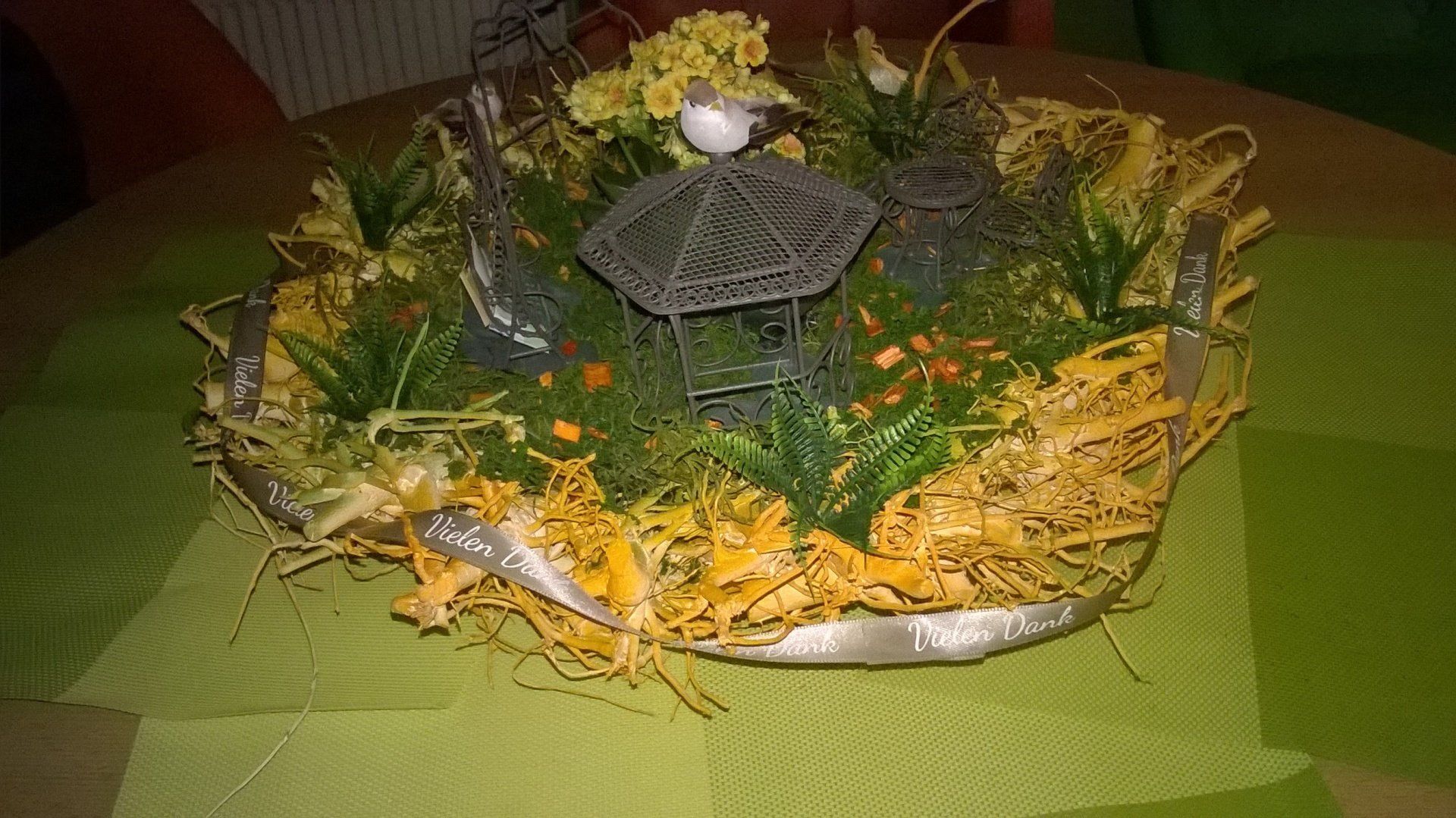 Ein Vogelkäfig ist von Blumen und Gras umgeben auf einem Tisch.