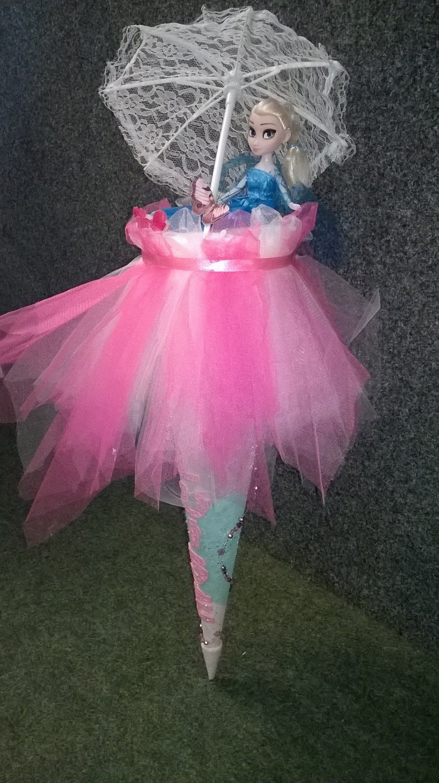 Eine Puppe sitzt mit einem Regenschirm auf einer rosa Blume.