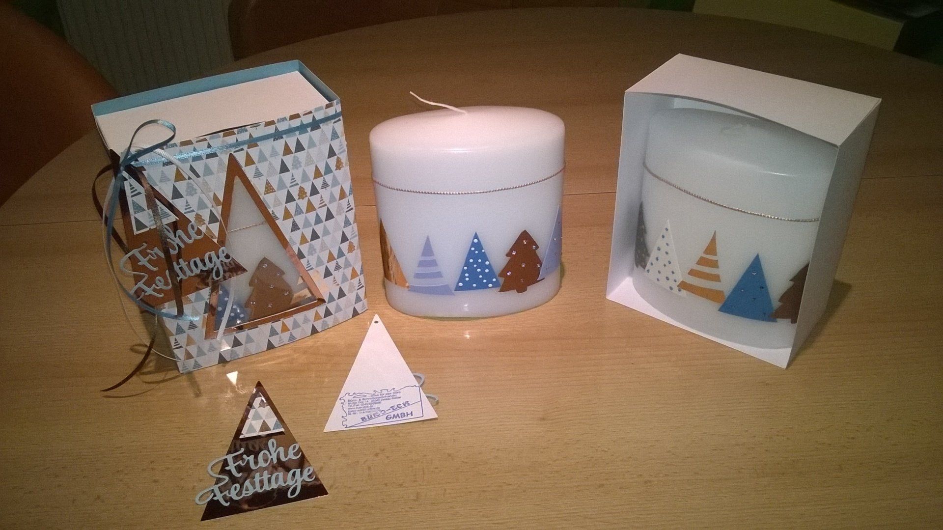 Zwei Kerzen stehen auf einem Tisch neben einer Karte mit der Aufschrift „Frohe Weihnachten“