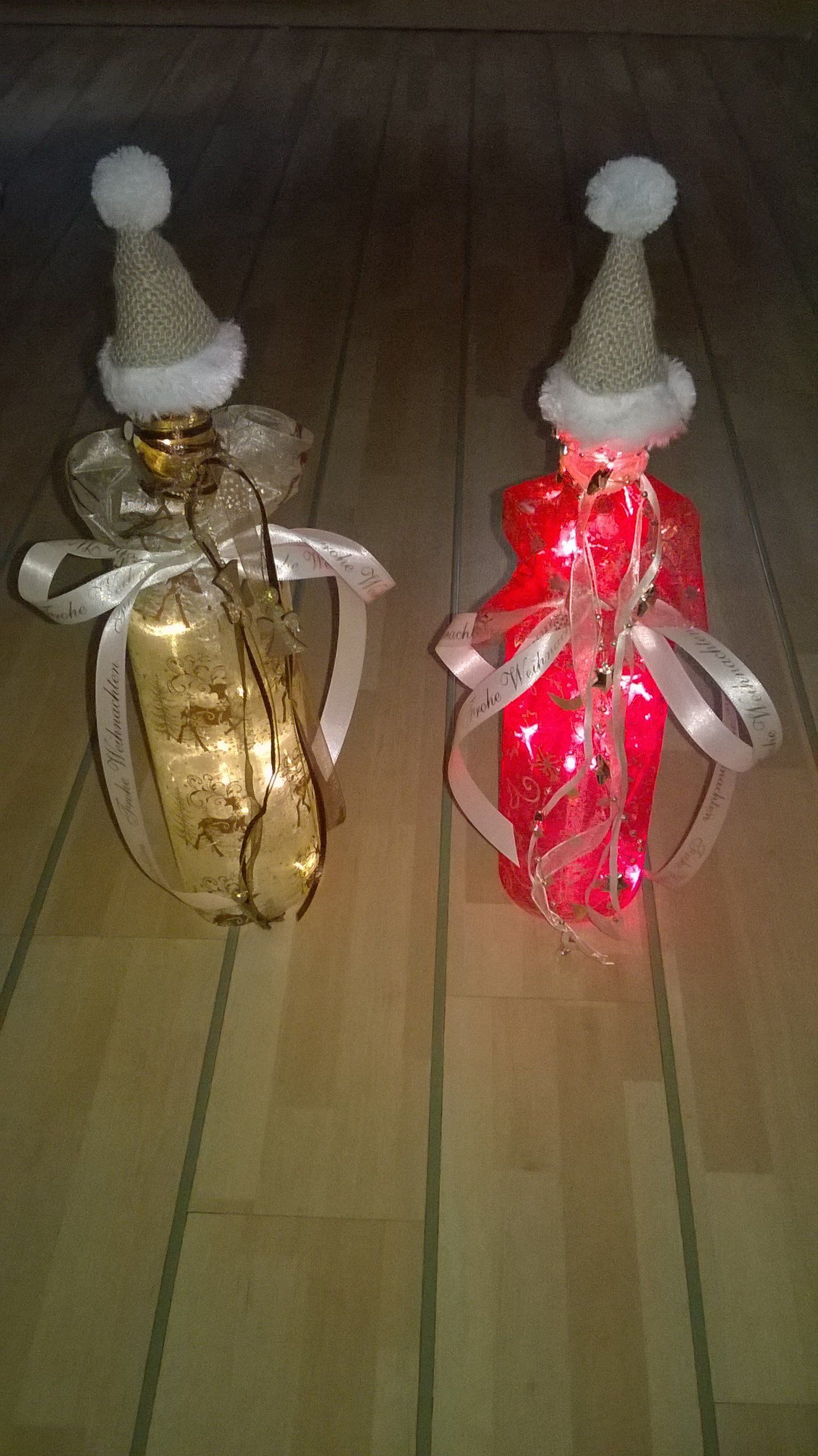 Zwei Flaschen mit Weihnachtsmannmützen darauf stehen auf einem Holzboden.
