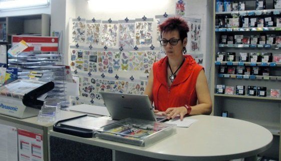 Eine Frau im roten Hemd sitzt mit einem Laptop an einem Schreibtisch
