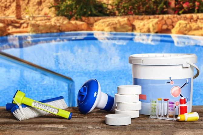 Pool cleaning supplies and chemicals beside a swimming pool, including buckets, brushes, and bottles.