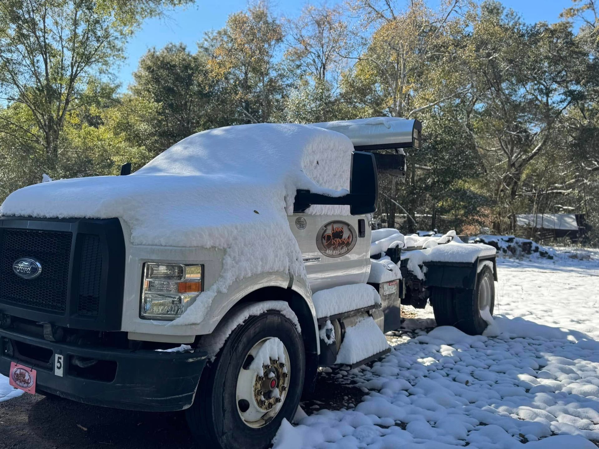 Snow-covered white semi-truck parked outdoors in a snowy wooded area Snow-covered white semi-truck parked outdoors in a snowy wooded area