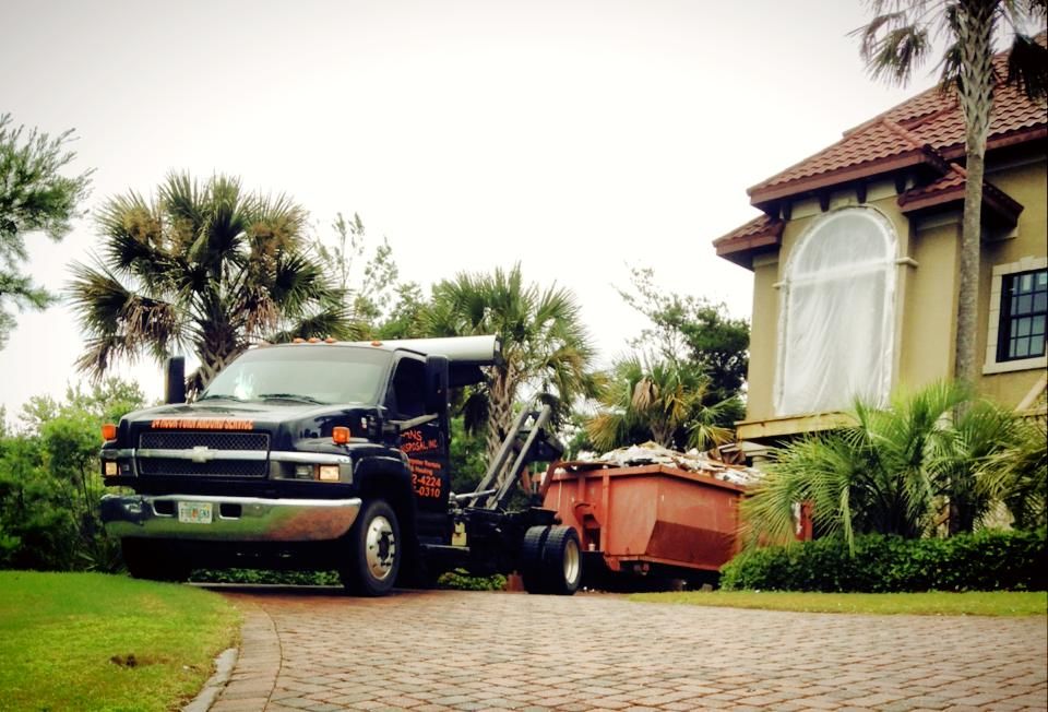 Tow truck hauling a dumpster beside a house with palm trees and a tiled driveway Tow truck hauling a dumpster beside a house with palm trees and a tiled driveway