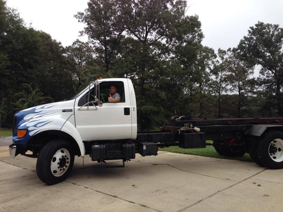 White truck chassis on a driveway with a driver in the cab, trees in the background. White truck chassis on a driveway with a driver in the cab, trees in the background.