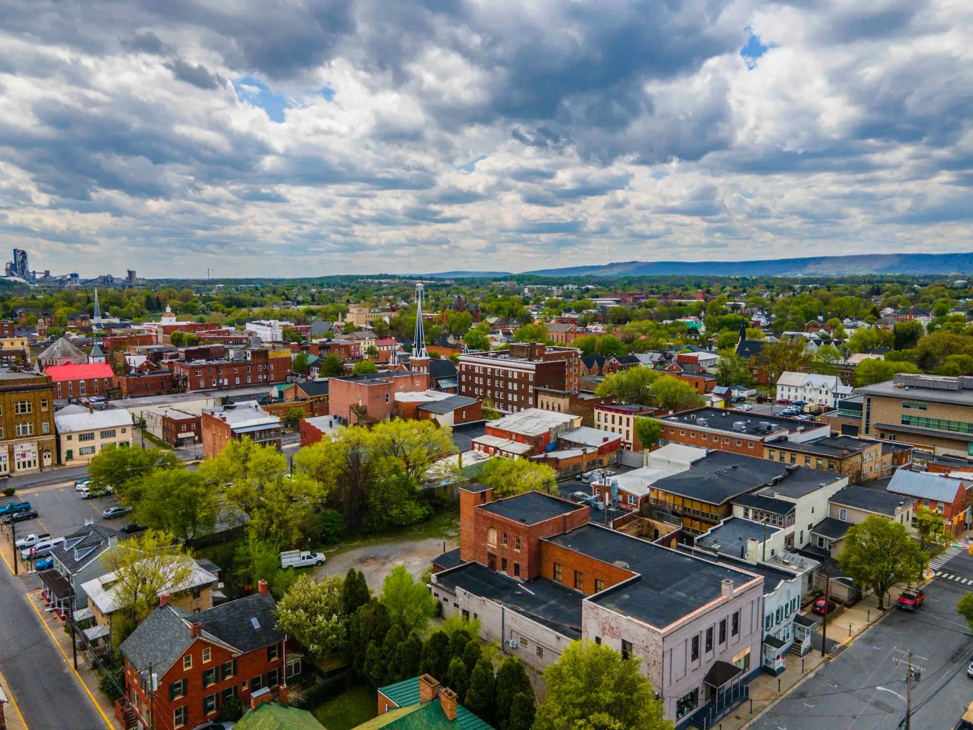 Aerial view of a town with red brick buildings, green trees, and cloudy sky.