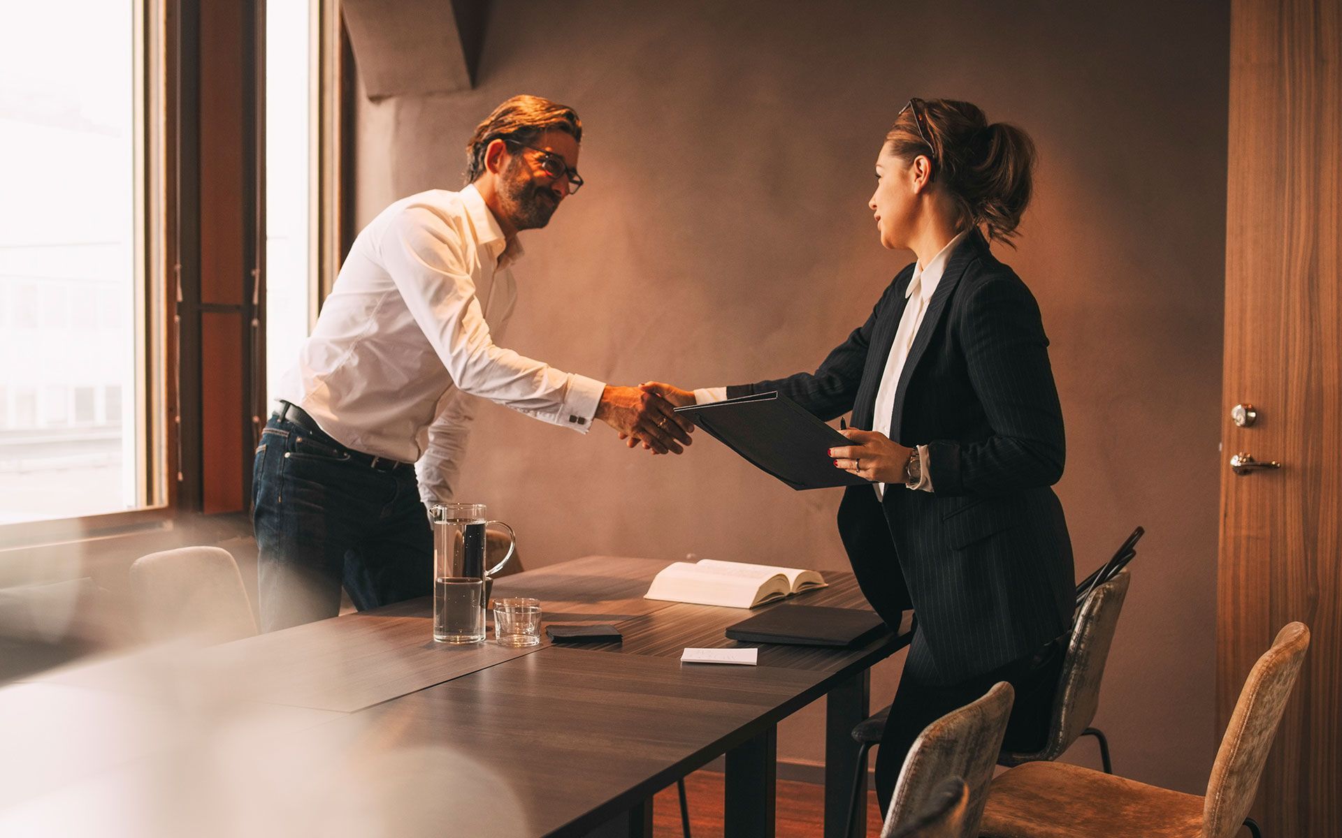 A man and a woman are shaking hands in a conference room.