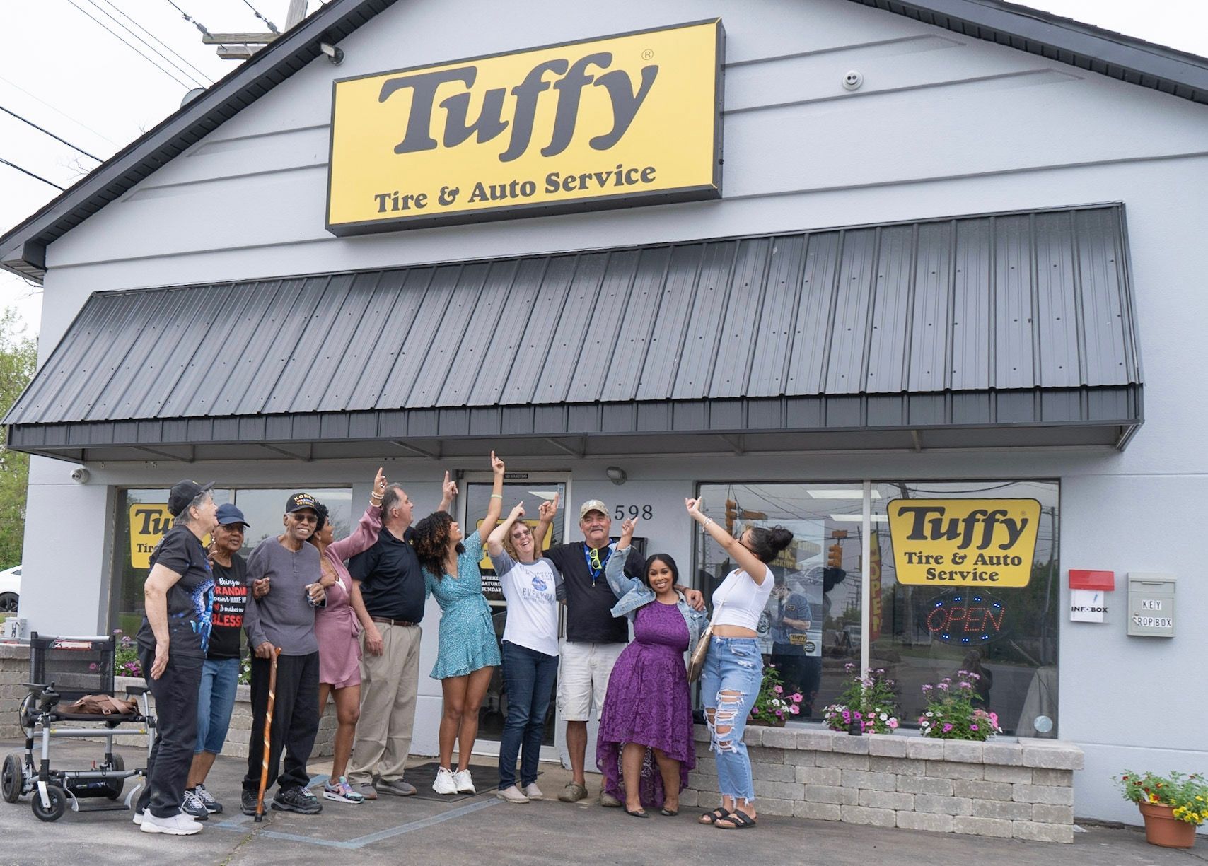 Group of people celebrating outside Tuffy Tire & Auto Service. They are pointing upward.