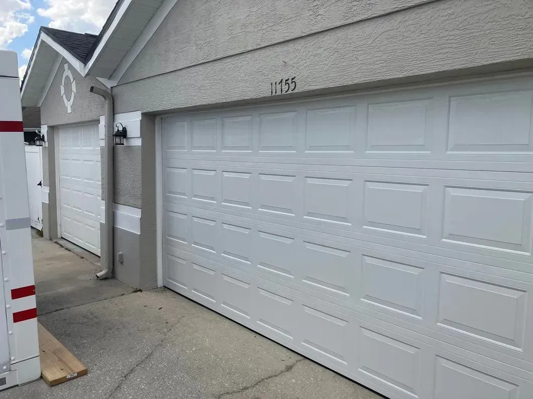 White garage doors on a building, a partially visible wooden object on the left, and a paved area in front.
