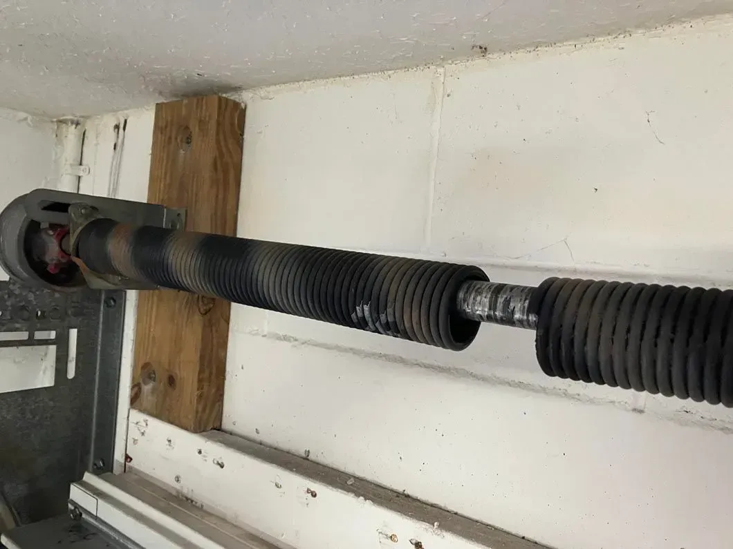 Garage door torsion spring, coiled, with rust and wear, mounted horizontally.