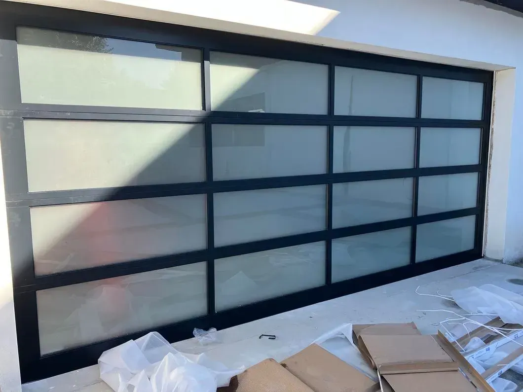 Black-framed glass garage door with frosted panels. Outdoors, with construction debris in front.