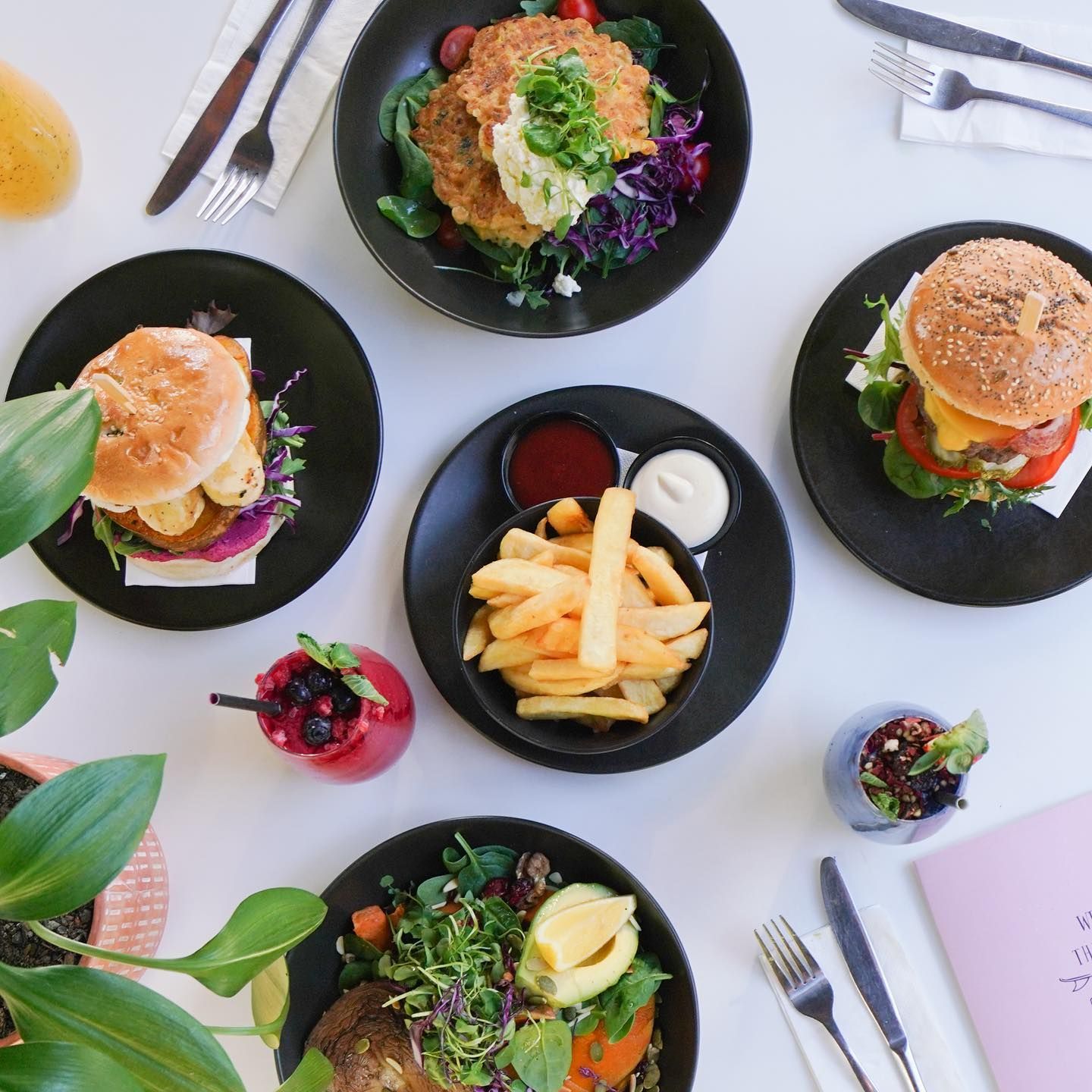 A Table Topped With Plates of Food Including Hamburgers and French Fries — The Pass Cafe in Byron Bay, NSW