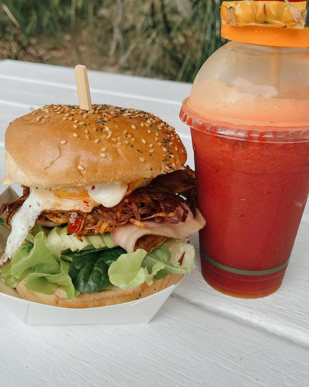 A Brekkie Burger Next to a Fruit Smoothie in a Plastic Takeaway Cup — The Pass Cafe in Byron Bay, NSW