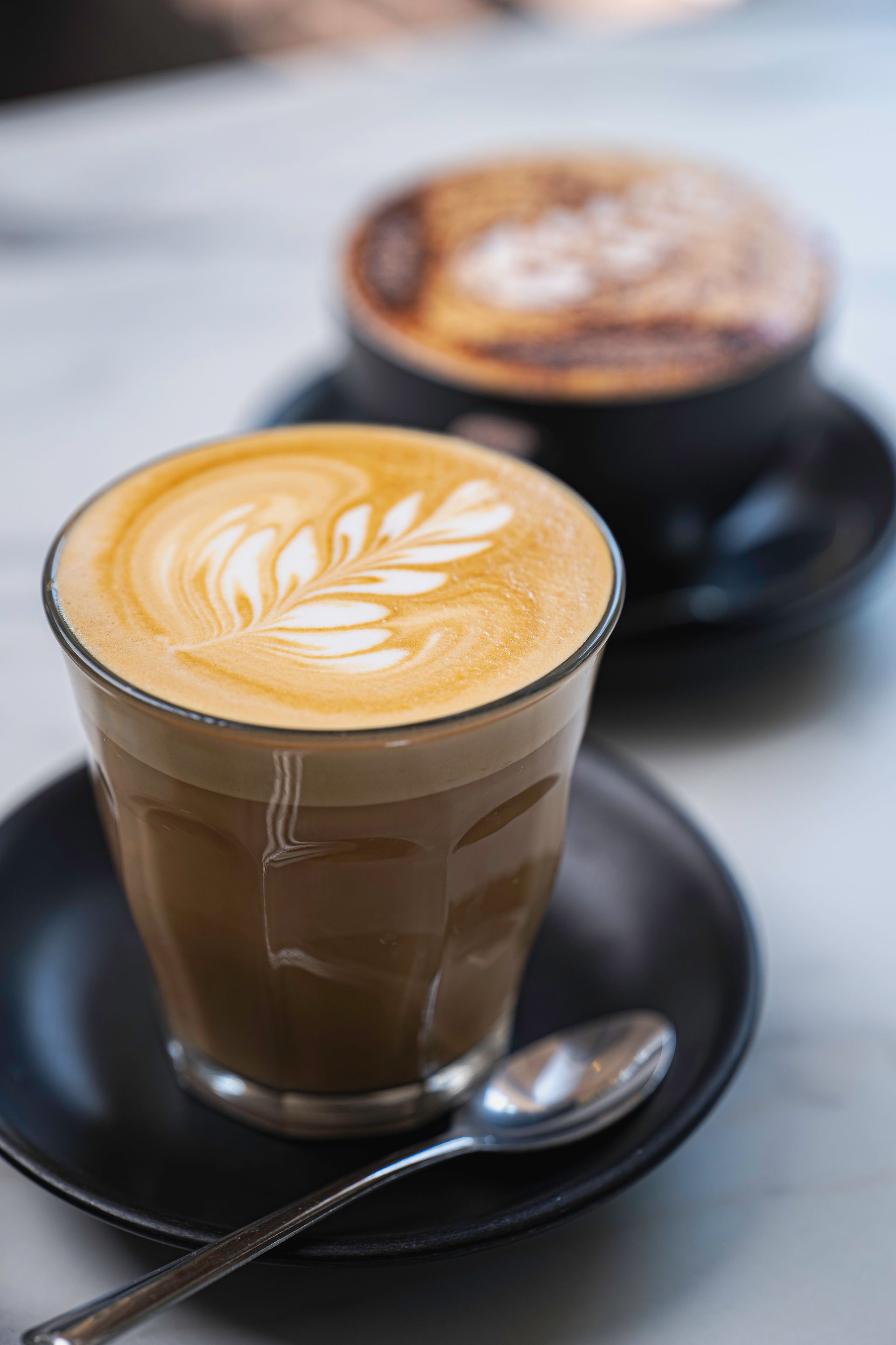 A Close Up of a Cup of Cappuccino on a Saucer With a Spoon — The Pass Cafe In Byron Bay, NSW