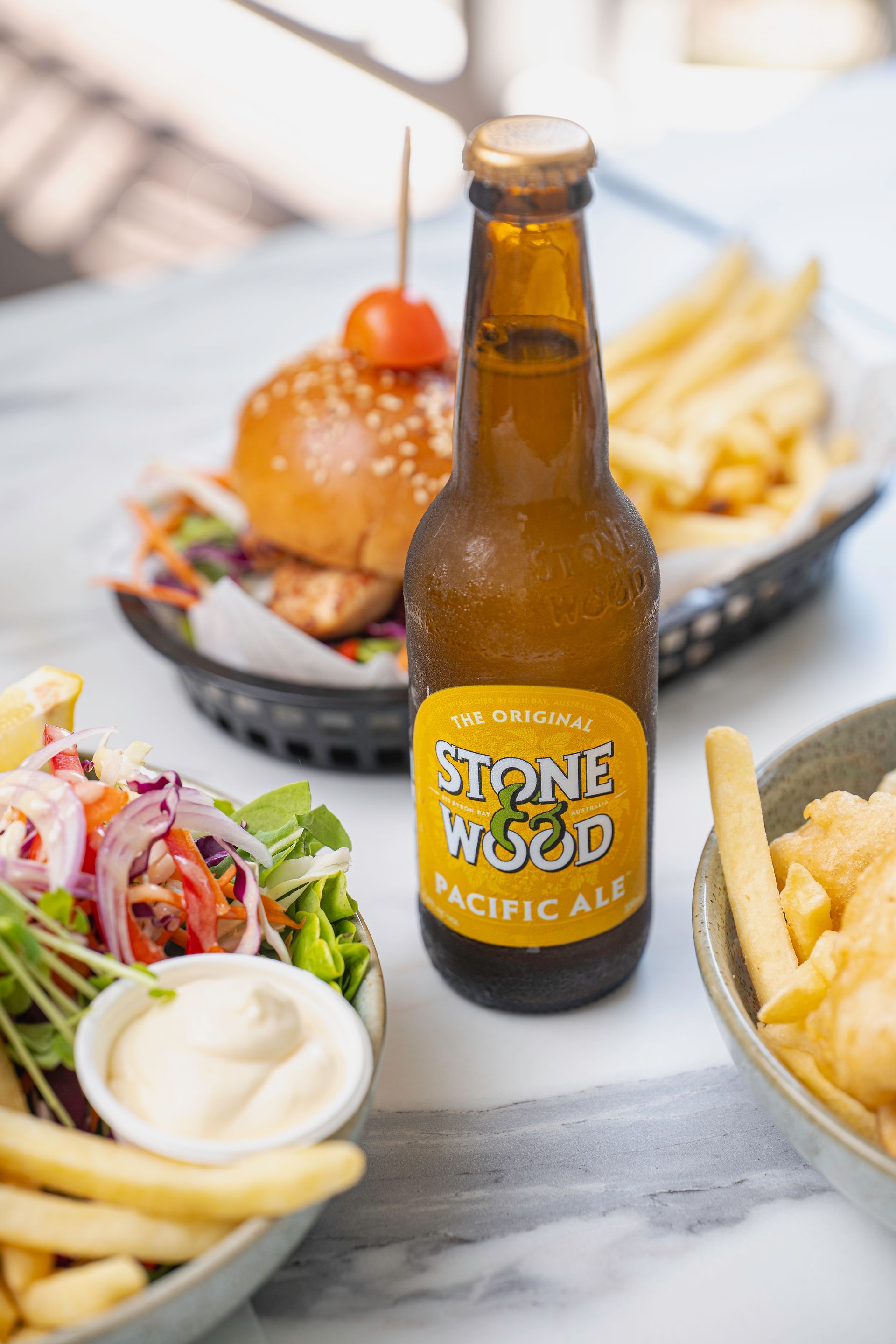 A Bottle of Stone Wood Pacific Ale is Sitting on a Table Next to a Salad and French Fries — The Pass Cafe In Byron Bay, NSW