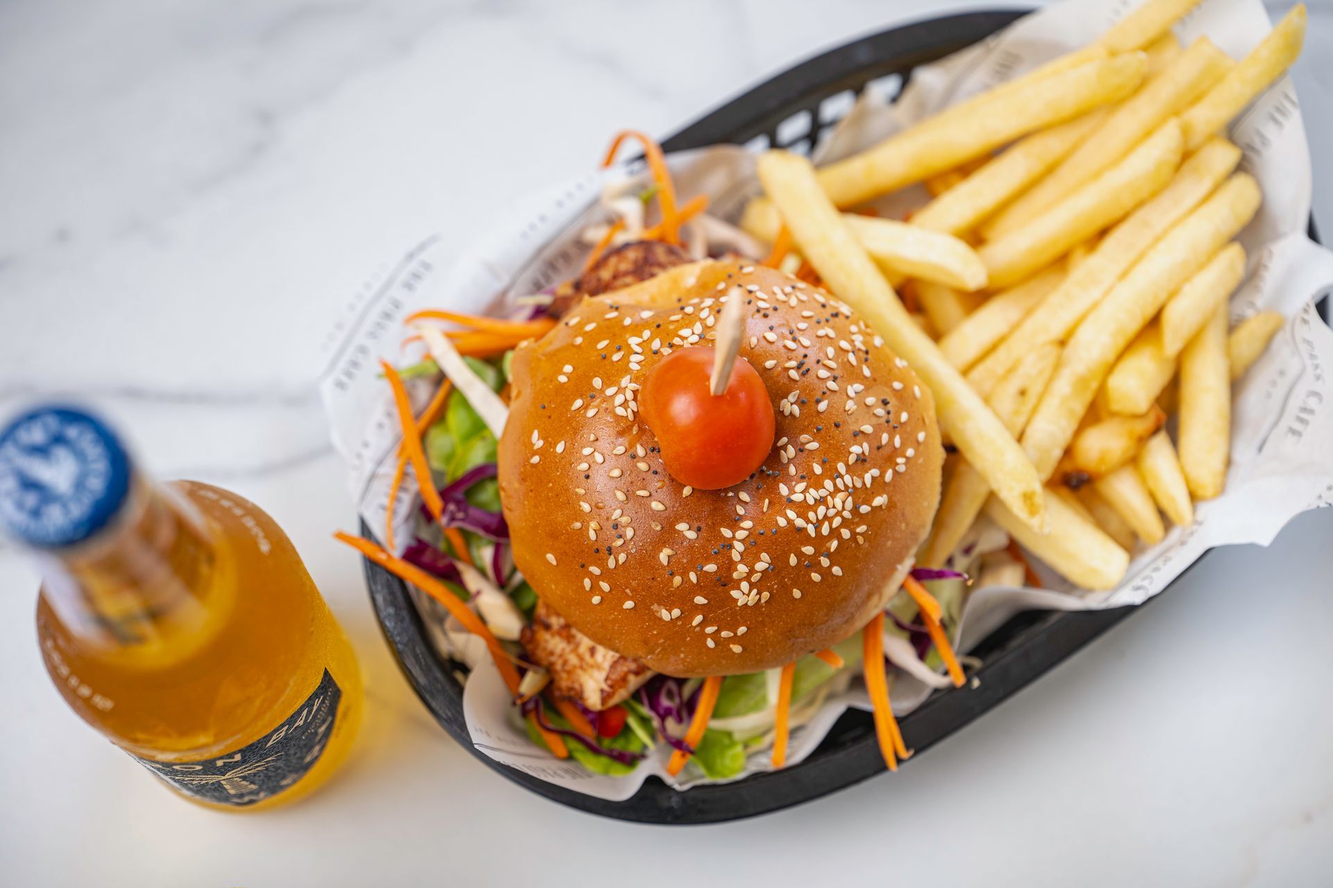 A Hamburger and French Fries in a Basket Next to a Bottle of Beer — The Pass Cafe In Byron Bay, NSW