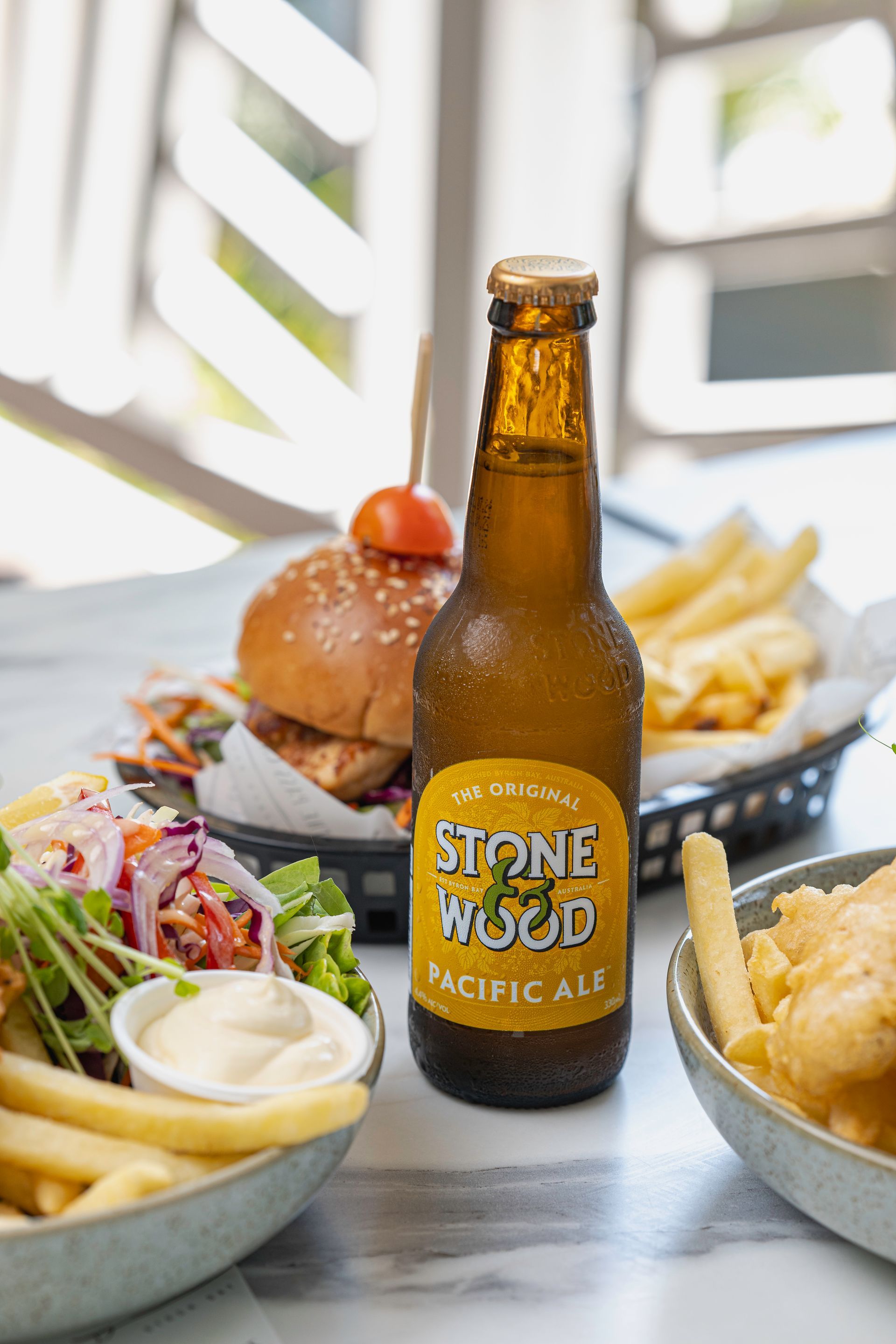A Bottle of Stone Wood Beer is Sitting on a Table Next to a Plate of Food — The Pass Cafe In Byron Bay, NSW