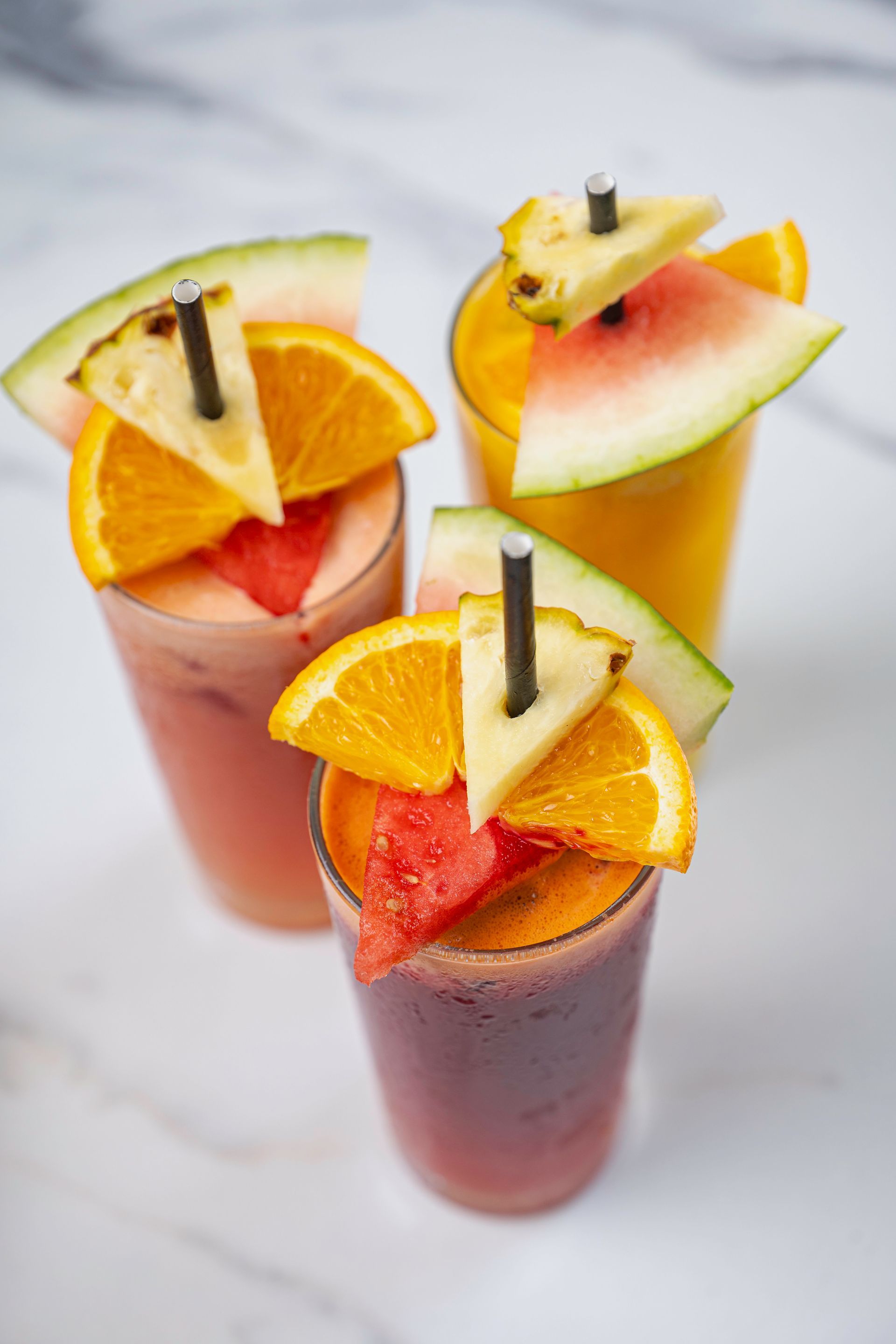 Three Glasses of Fruit Smoothies With Watermelon, Orange Slices and Pineapple Slices on a Table — The Pass Cafe In Byron Bay, NSW