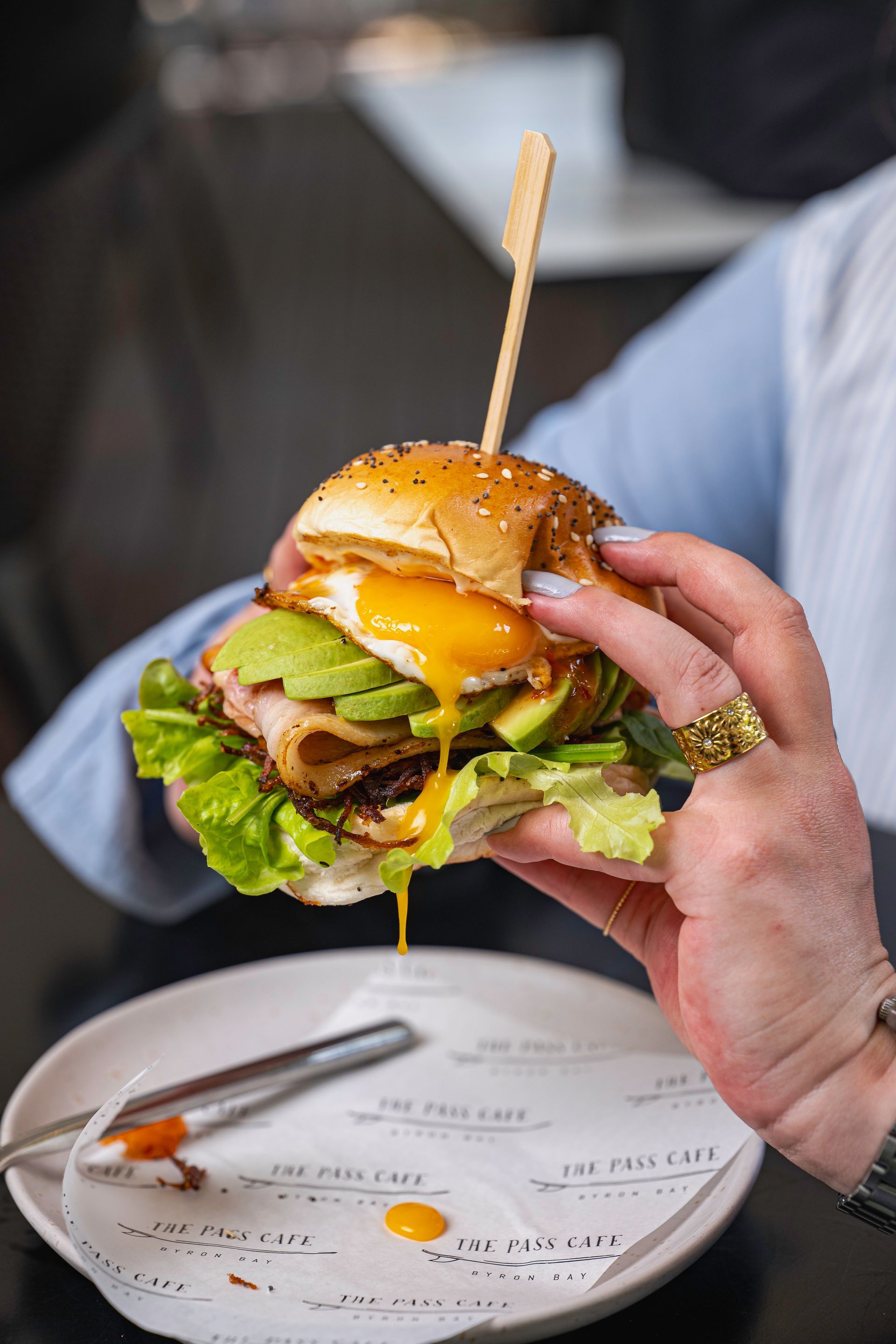 A Person is Holding a Sandwich With a Toothpick in Their Hand — The Pass Cafe In Byron Bay, NSW