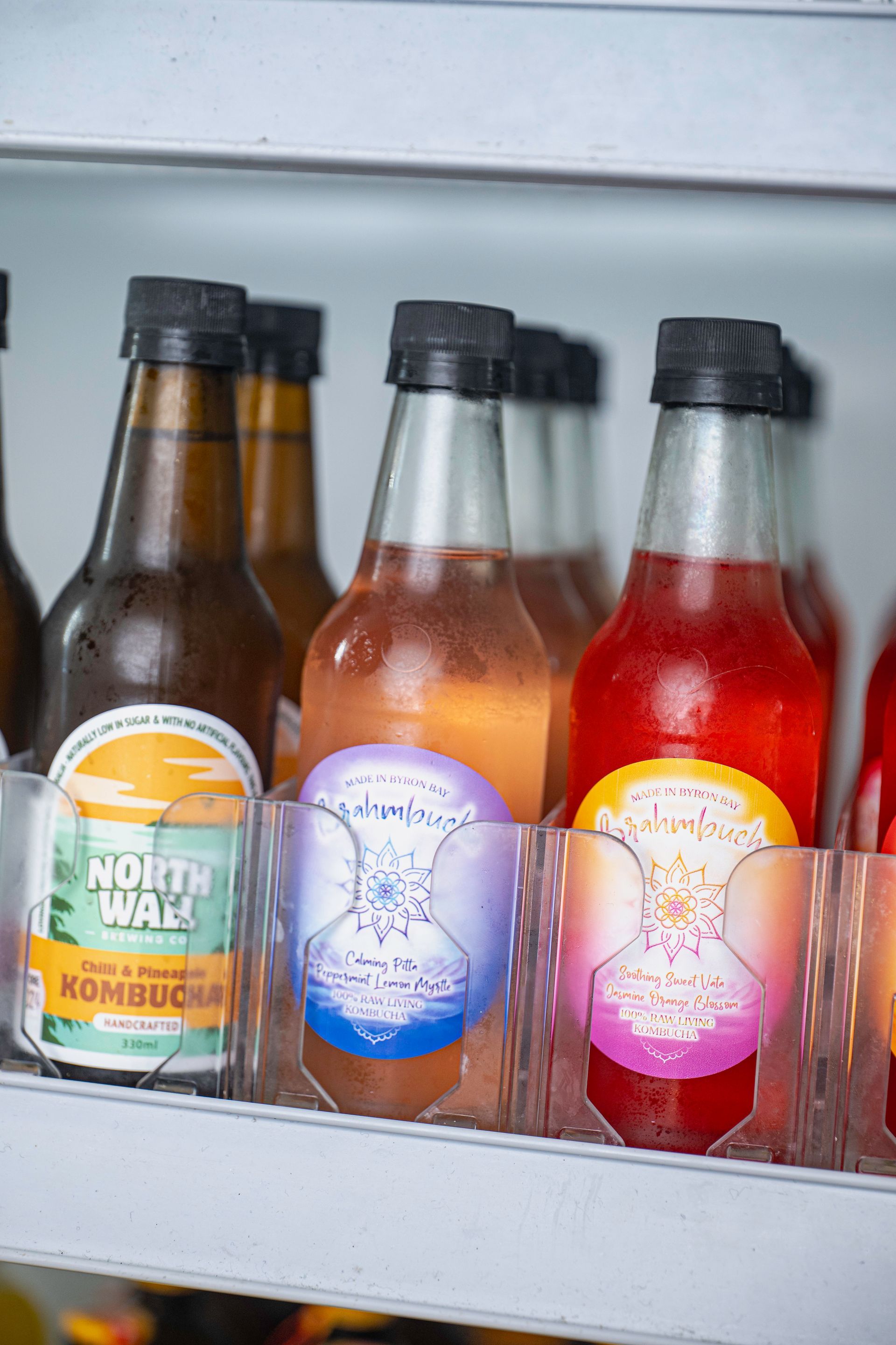 Bottles of Kombucha Are Lined Up on a Shelf in a Refrigerator — The Pass Cafe In Byron Bay, NSW