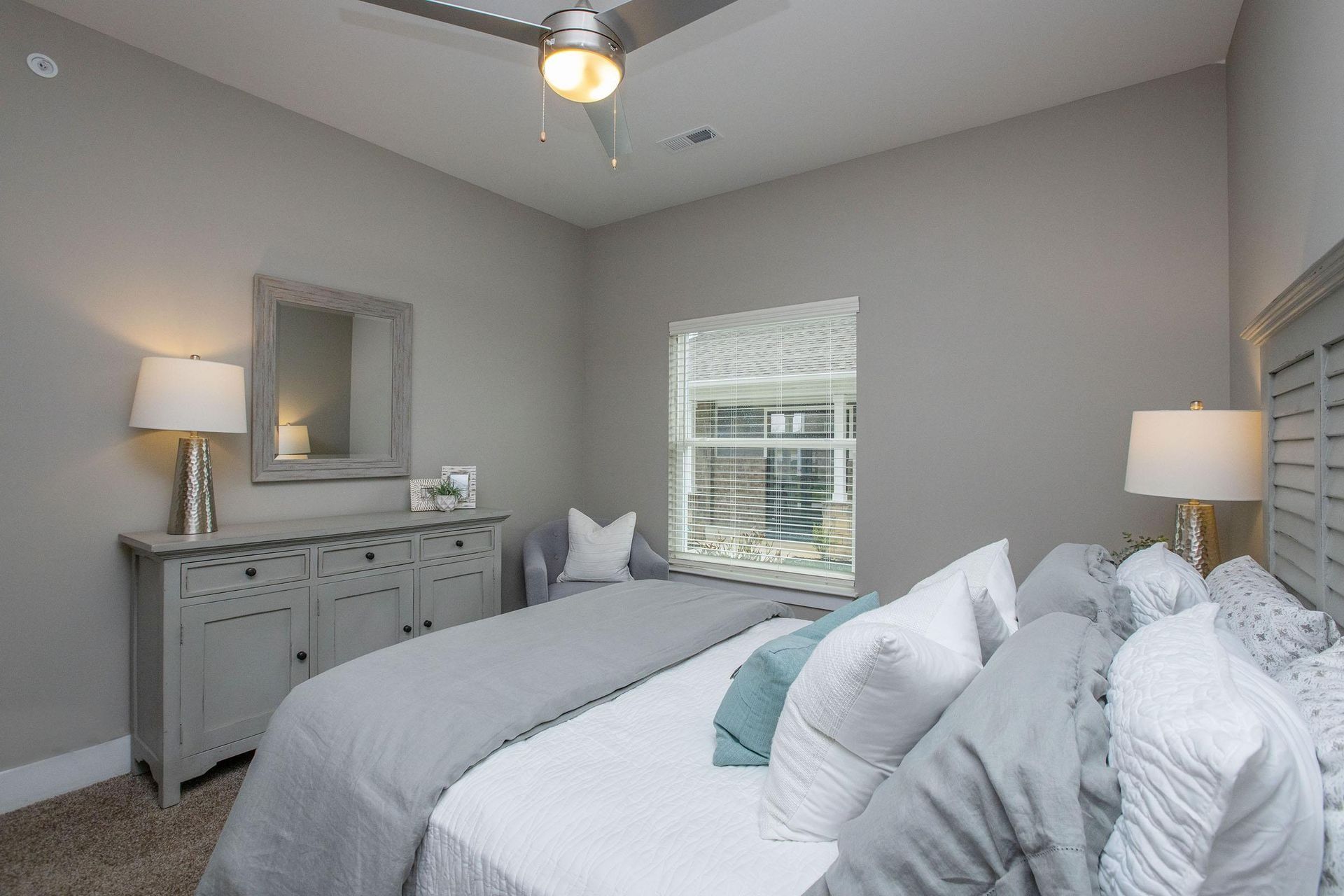 Bedroom with gray walls, bed, dresser, window, and lamps.