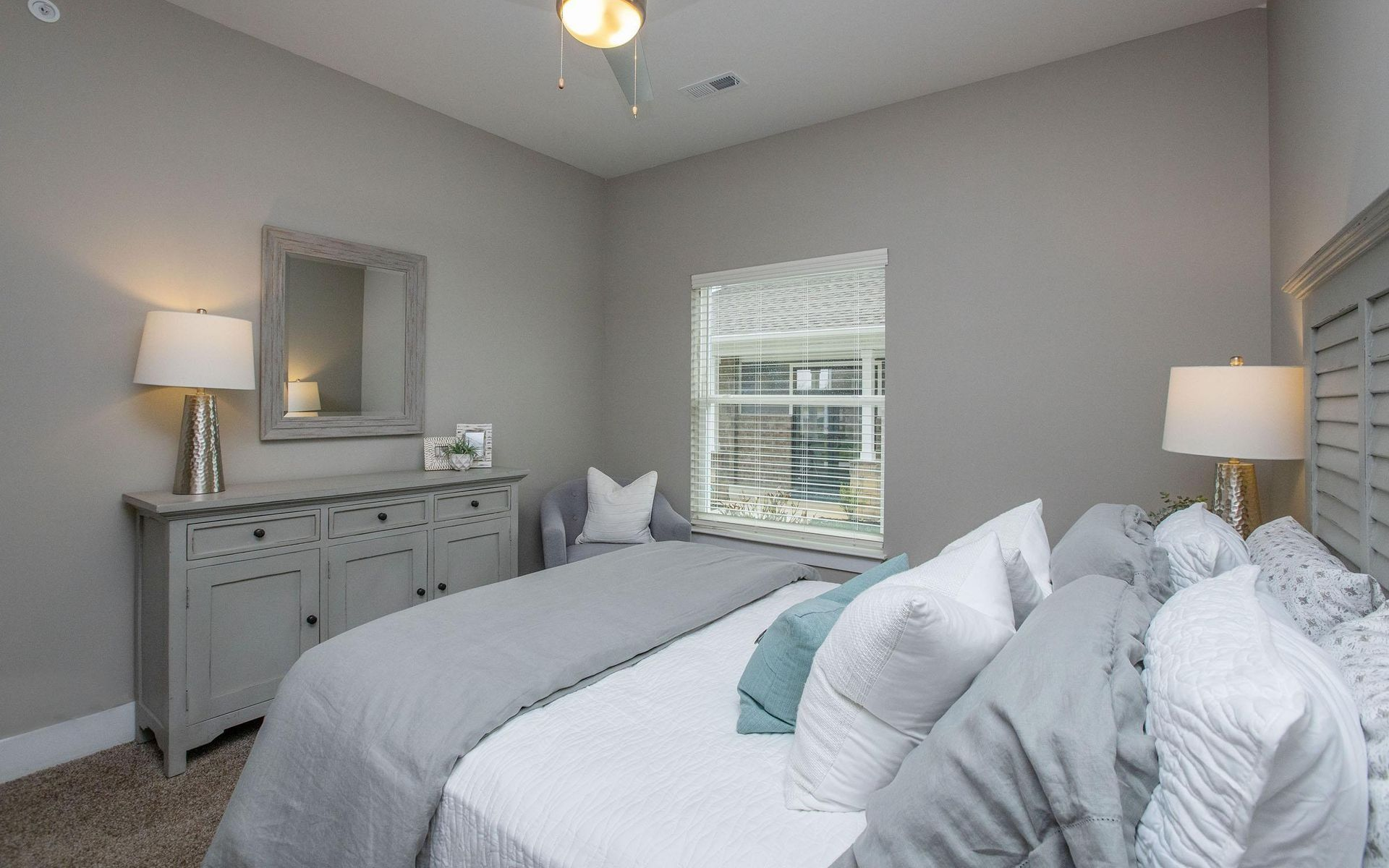 Bedroom with gray walls, bed, dresser, window, and lamps.