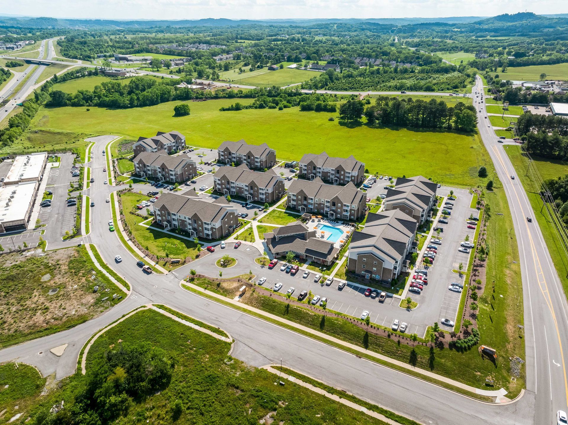 Aerial view of an apartment complex surrounded by roads and a field, with a pool in the center.