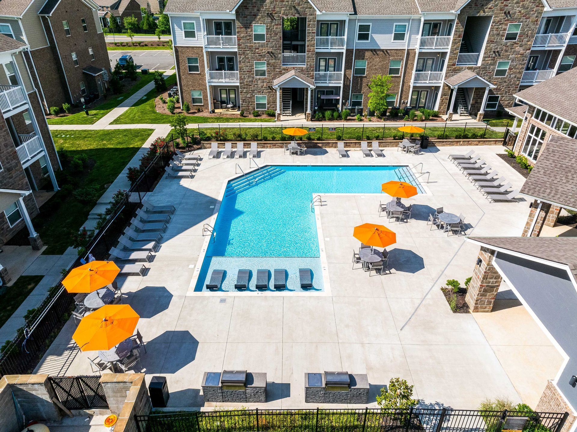 Apartment complex with pool, orange umbrellas, and barbecue grills.