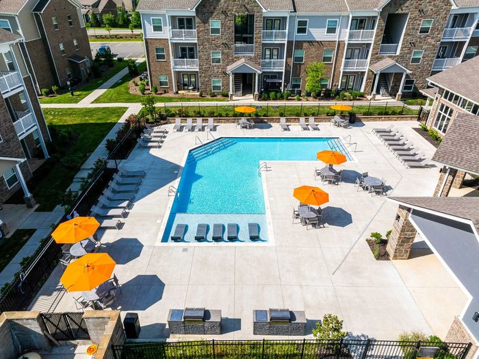 Apartment complex with pool, orange umbrellas, and barbecue grills.