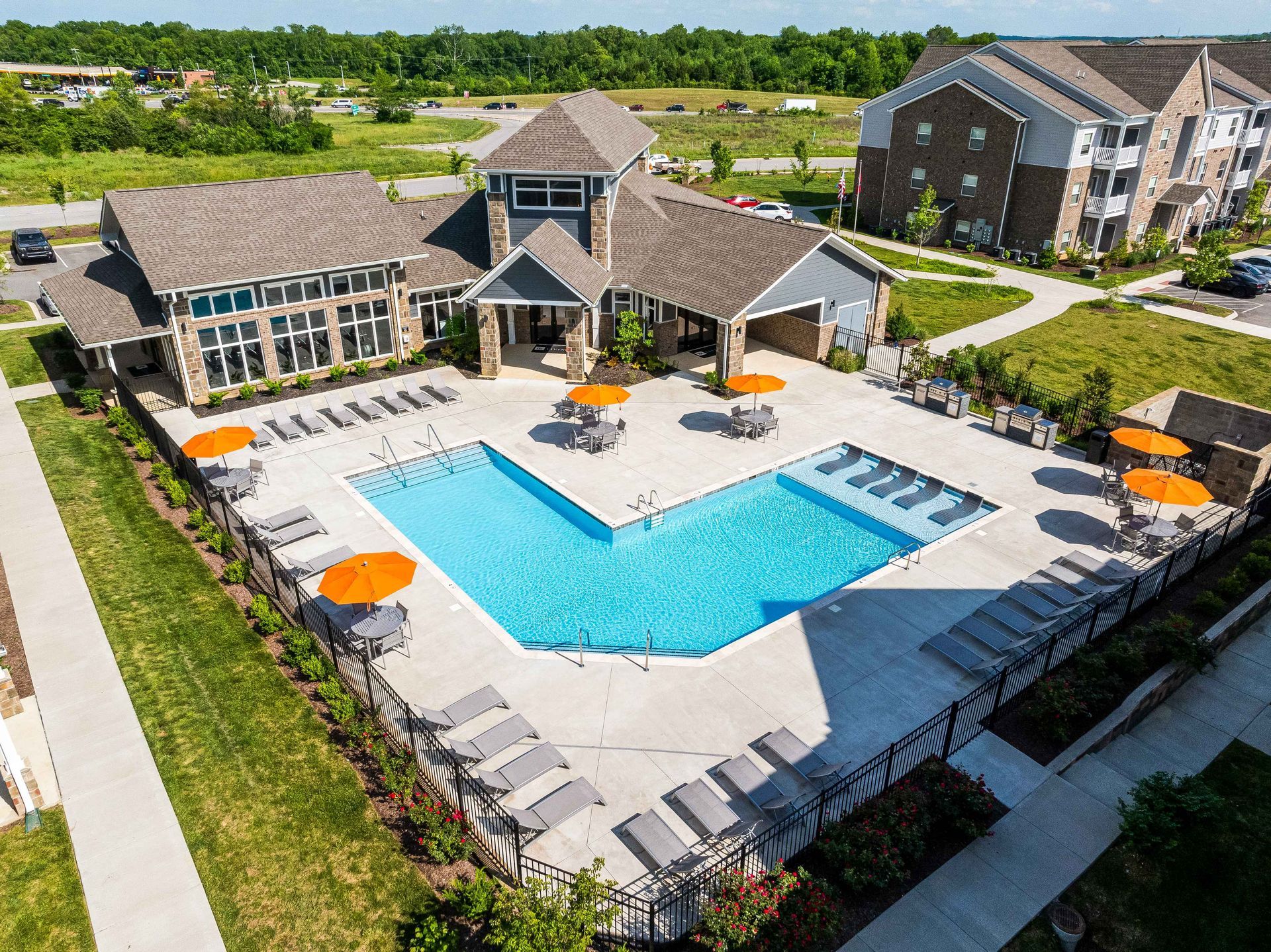 Aerial view of a blue swimming pool, lounge chairs, and an apartment complex clubhouse with orange umbrellas.