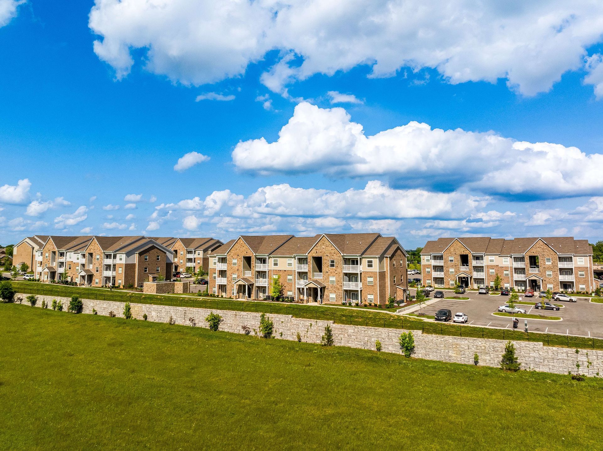 Apartment buildings with tan brick and brown roofs under a bright blue sky with fluffy white clouds.