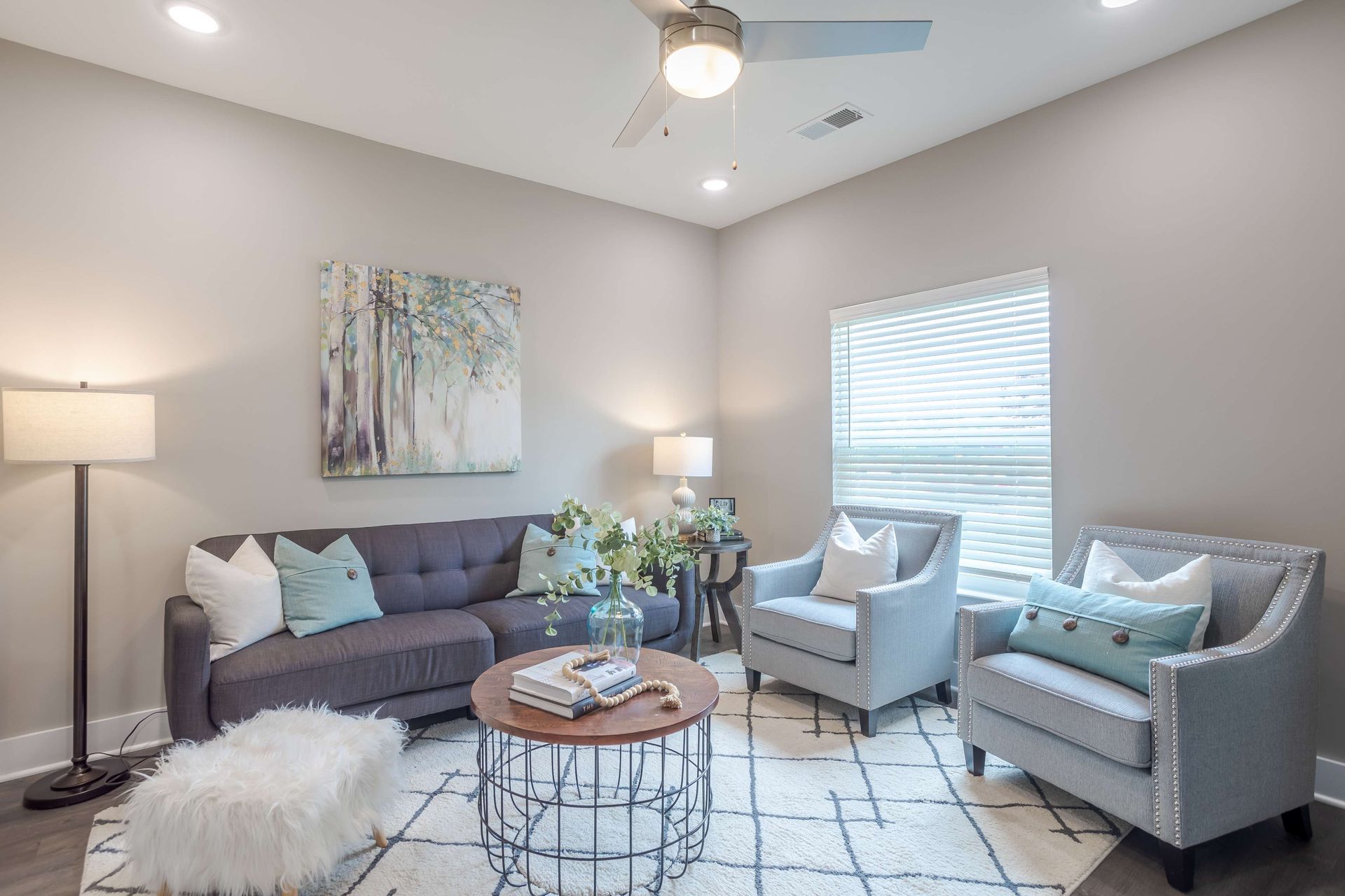 Living room with gray couch, two armchairs, rug, artwork, and a coffee table.