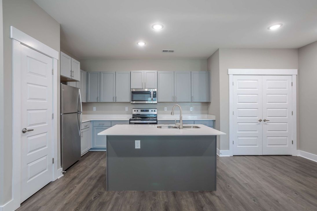 Modern kitchen with gray cabinets, island, stainless steel appliances, and wood-look flooring.
