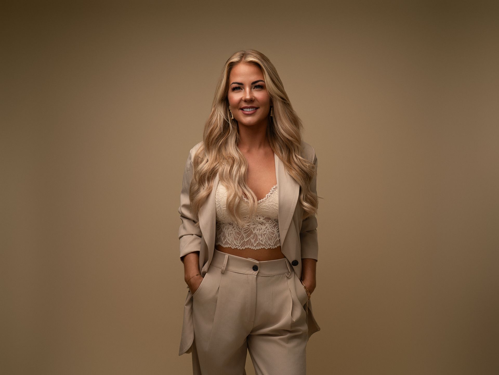 Een vrouw in een pak en een crop top staat met haar handen in haar zakken.