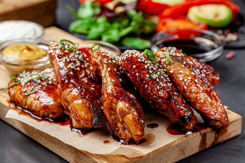 Chicken wings with sesame seeds, served on a wooden board with dipping sauces and vegetables.