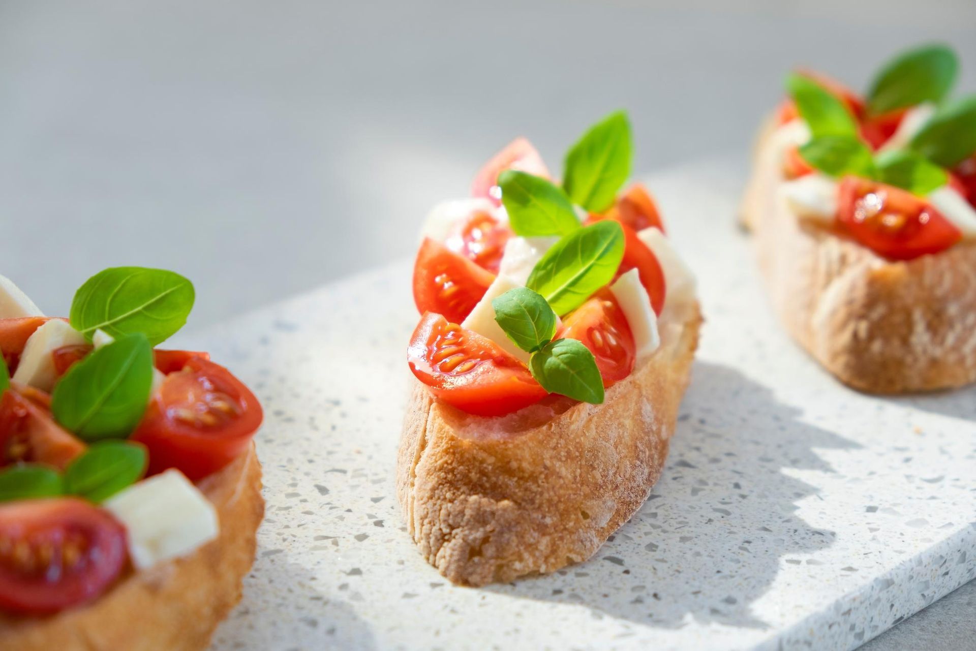 Bruschetta with tomatoes, mozzarella, and basil on a white serving board.