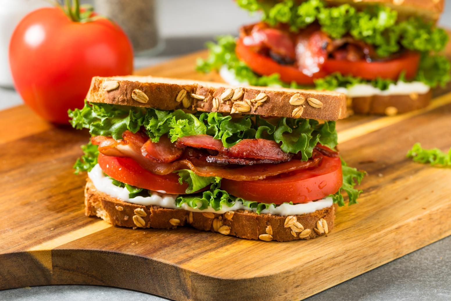 BLT sandwich with bacon, lettuce, and tomato on toasted bread, with a whole tomato nearby.