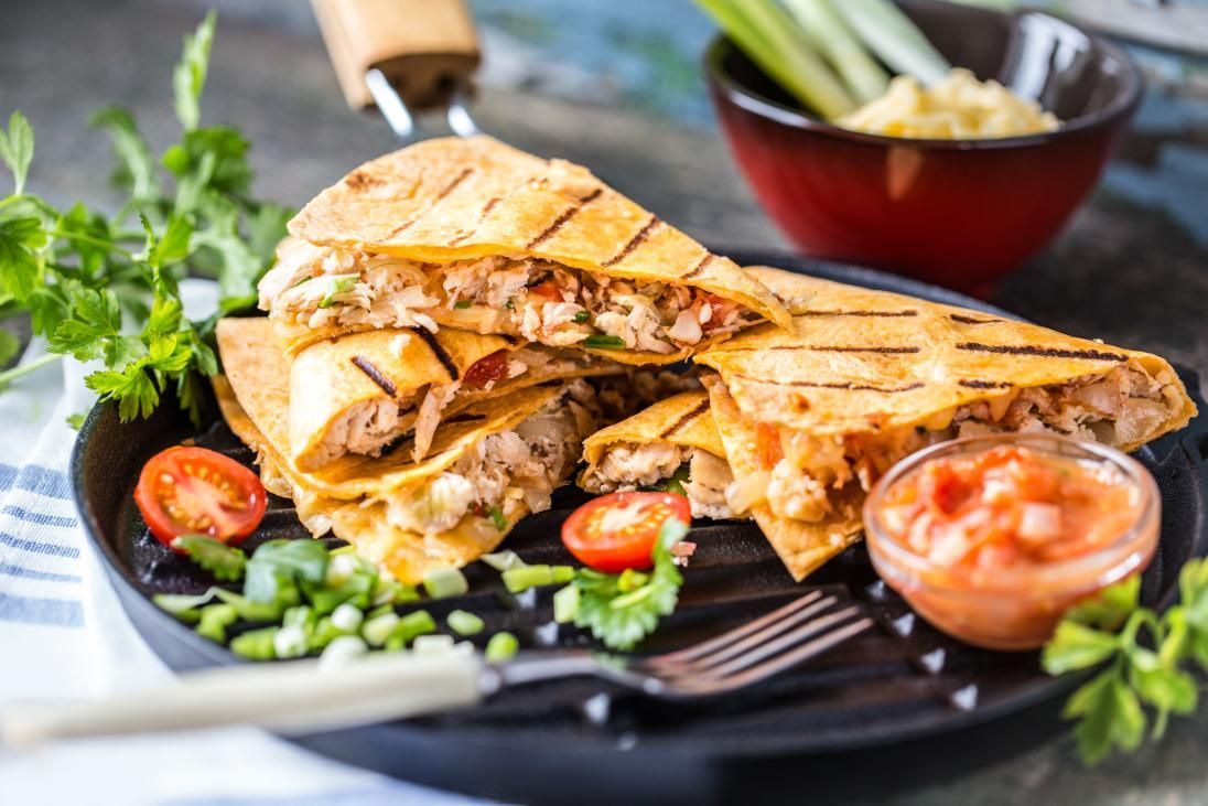 Grilled chicken quesadillas with salsa, tomatoes, and parsley on a black grill pan.
