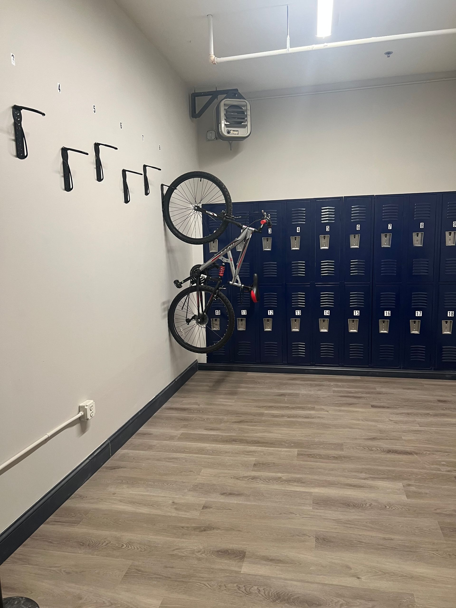 Bike storage room with wall-mounted bike hooks, lockers, a bike, and wood-look flooring.