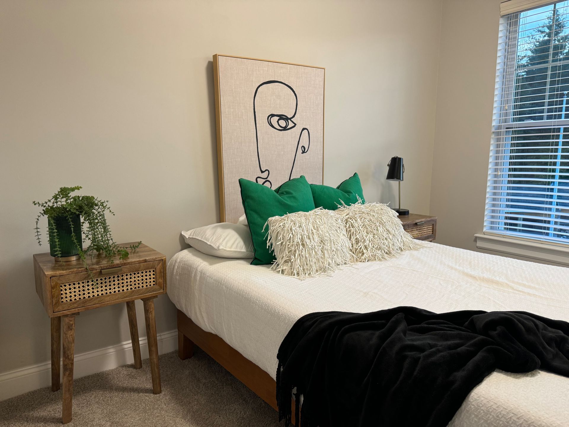 Bedroom with white bed, green pillows, black throw, nightstand, and window with blinds.